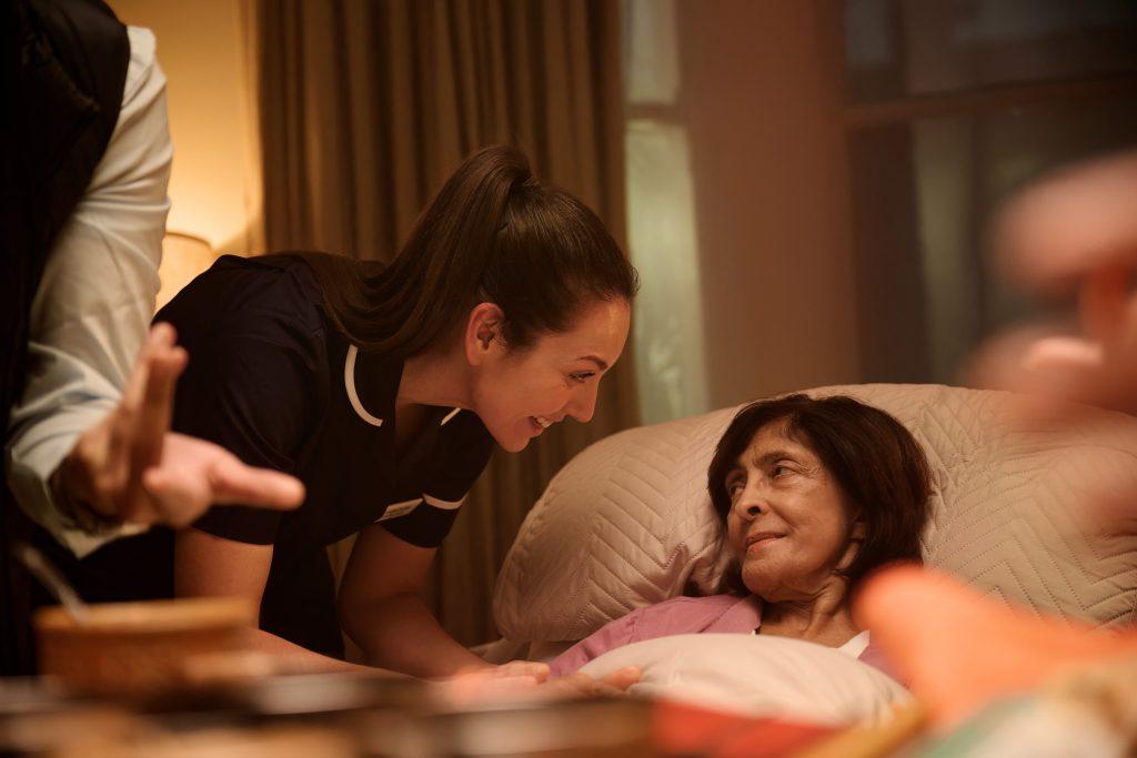 Nurse attending to lady in bed at home.